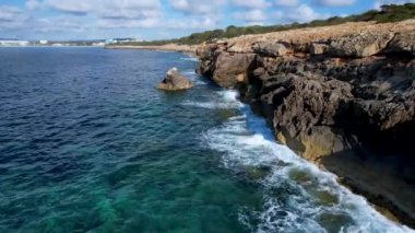 4K Hava Aracı 'nın Mallorca' da kristal berrak suyla çekilmiş videosu güneşli bir yaz gününde sert dalgalar kayalıklara çarpıyor.