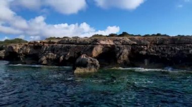 4K Hava Aracı 'nın Mallorca' da kristal berrak suyla çekilmiş videosu güneşli bir yaz gününde sert dalgalar kayalıklara çarpıyor.