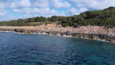 4K Hava Aracı 'nın Mallorca' da kristal berrak suyla çekilmiş videosu güneşli bir yaz gününde sert dalgalar kayalıklara çarpıyor.