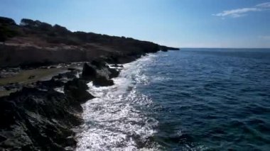 4K Hava Aracı 'nın Mallorca' da kristal berrak suyla çekilmiş videosu güneşli bir yaz gününde sert dalgalar kayalıklara çarpıyor.