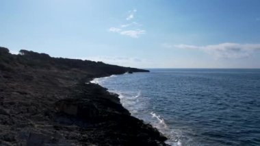 4K Hava Aracı 'nın Mallorca' da kristal berrak suyla çekilmiş videosu güneşli bir yaz gününde sert dalgalar kayalıklara çarpıyor.
