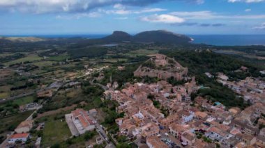 4K Hava Aracı, güneşli bir yaz gününde dağlarla ve denizlerle çevrili tepede devasa bir kalesi olan güzel bir terracotta renkli kasabasının videosu, Capdepera, Mallorca