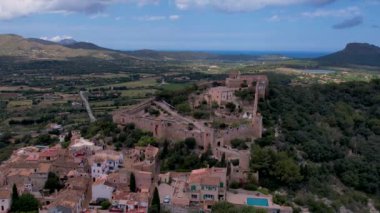 4K Hava Aracı, güneşli bir yaz gününde dağlarla ve denizlerle çevrili tepede devasa bir kalesi olan güzel bir terracotta renkli kasabasının videosu, Capdepera, Mallorca