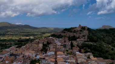4K Hava Aracı, güneşli bir yaz gününde dağlarla ve denizlerle çevrili tepede devasa bir kalesi olan güzel bir terracotta renkli kasabasının videosu, Capdepera, Mallorca