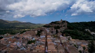 4K Hava Aracı, güneşli bir yaz gününde dağlarla ve denizlerle çevrili tepede devasa bir kalesi olan güzel bir terracotta renkli kasabasının videosu, Capdepera, Mallorca