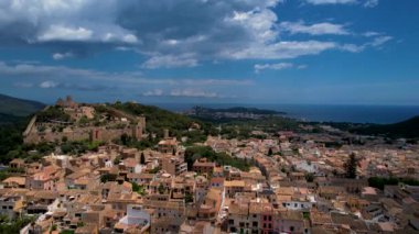 4K Hava Aracı, güneşli bir yaz gününde dağlarla ve denizlerle çevrili tepede devasa bir kalesi olan güzel bir terracotta renkli kasabasının videosu, Capdepera, Mallorca