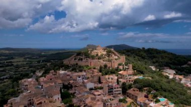 4K Hava Aracı, güneşli bir yaz gününde dağlarla ve denizlerle çevrili tepede devasa bir kalesi olan güzel bir terracotta renkli kasabasının videosu, Capdepera, Mallorca