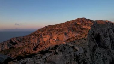 4K Aerial Drone 'un geniş deniz ufkundan yükselen ateşli kırmızı gündoğumu videosu kayalıkların kenarındaki deniz feneri Far of Cap de Formentor, Mallorca, İspanya
