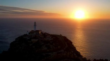 4K Aerial Drone 'un geniş deniz ufkundan yükselen ateşli kırmızı gündoğumu videosu kayalıkların kenarındaki deniz feneri Far of Cap de Formentor, Mallorca, İspanya