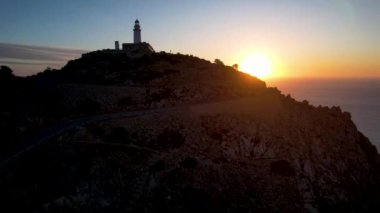 4K Aerial Drone 'un geniş deniz ufkundan yükselen ateşli kırmızı gündoğumu videosu kayalıkların kenarındaki deniz feneri Far of Cap de Formentor, Mallorca, İspanya
