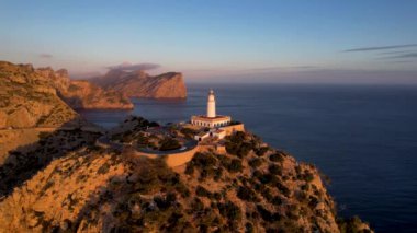 4K Aerial Drone 'un geniş deniz ufkundan yükselen ateşli kırmızı gündoğumu videosu kayalıkların kenarındaki deniz feneri Far of Cap de Formentor, Mallorca, İspanya