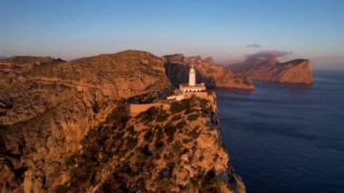 4K Aerial Drone 'un geniş deniz ufkundan yükselen ateşli kırmızı gündoğumu videosu kayalıkların kenarındaki deniz feneri Far of Cap de Formentor, Mallorca, İspanya