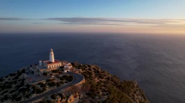 4K Aerial Drone 'un geniş deniz ufkundan yükselen ateşli kırmızı gündoğumu videosu kayalıkların kenarındaki deniz feneri Far of Cap de Formentor, Mallorca, İspanya