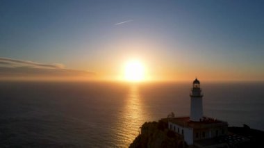 4K Aerial Drone 'un geniş deniz ufkundan yükselen ateşli kırmızı gündoğumu videosu kayalıkların kenarındaki deniz feneri Far of Cap de Formentor, Mallorca, İspanya