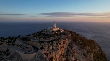 4K Aerial Drone 'un geniş deniz ufkundan yükselen ateşli kırmızı gündoğumu videosu kayalıkların kenarındaki deniz feneri Far of Cap de Formentor, Mallorca, İspanya
