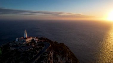 4K Aerial Drone 'un geniş deniz ufkundan yükselen ateşli kırmızı gündoğumu videosu kayalıkların kenarındaki deniz feneri Far of Cap de Formentor, Mallorca, İspanya