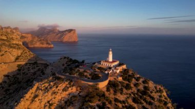 4K Aerial Drone 'un geniş deniz ufkundan yükselen ateşli kırmızı gündoğumu videosu kayalıkların kenarındaki deniz feneri Far of Cap de Formentor, Mallorca, İspanya