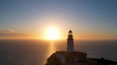 4K Aerial Drone 'un geniş deniz ufkundan yükselen ateşli kırmızı gündoğumu videosu kayalıkların kenarındaki deniz feneri Far of Cap de Formentor, Mallorca, İspanya