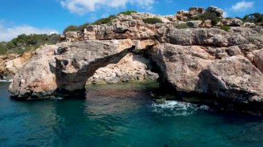 4K Hava Aracı 'nın eşsiz bir kaya oluşumunun videosu. Kayalıklardan ayrılan bir kemer. Yakınındaki turkuaz berrak mavi su ve plajla birlikte. Es Pontas, Mallorca