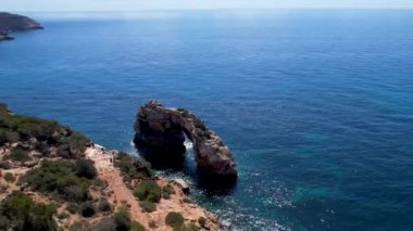 4K Hava Aracı 'nın eşsiz bir kaya oluşumunun videosu. Kayalıklardan ayrılan bir kemer. Yakınındaki turkuaz berrak mavi su ve plajla birlikte. Es Pontas, Mallorca
