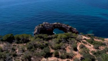 4K Hava Aracı 'nın eşsiz bir kaya oluşumunun videosu. Kayalıklardan ayrılan bir kemer. Yakınındaki turkuaz berrak mavi su ve plajla birlikte. Es Pontas, Mallorca