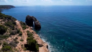 4K Hava Aracı 'nın eşsiz bir kaya oluşumunun videosu. Kayalıklardan ayrılan bir kemer. Yakınındaki turkuaz berrak mavi su ve plajla birlikte. Es Pontas, Mallorca