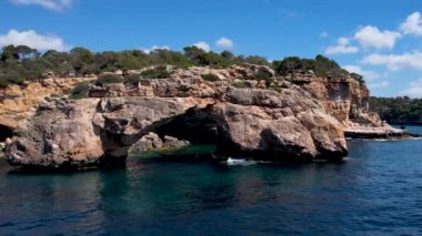 4K Hava Aracı 'nın eşsiz bir kaya oluşumunun videosu. Kayalıklardan ayrılan bir kemer. Yakınındaki turkuaz berrak mavi su ve plajla birlikte. Es Pontas, Mallorca