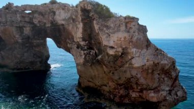 4K Hava Aracı 'nın eşsiz bir kaya oluşumunun videosu. Kayalıklardan ayrılan bir kemer. Yakınındaki turkuaz berrak mavi su ve plajla birlikte. Es Pontas, Mallorca