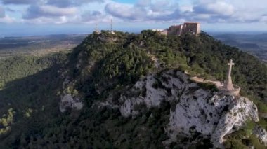 4K Hava Aracı video destansı heykel, tepenin üstünde çapraz ve manastır güneşli bir günde, Sant Salvador Sığınak ve Puig, Mallorca