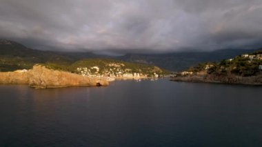 Popüler yaz mevsiminin 4K Aerial Drone videosu, uçurumların üzerinde gün batımı bir deniz feneri ve büyük bir liman dolusu martıların uçtuğu altın saat. Port de Soller, Mallorca