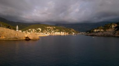 Popüler yaz mevsiminin 4K Aerial Drone videosu, uçurumların üzerinde gün batımı bir deniz feneri ve büyük bir liman dolusu martıların uçtuğu altın saat. Port de Soller, Mallorca