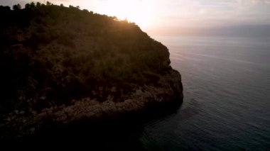 Popüler yaz mevsiminin 4K Aerial Drone videosu, uçurumların üzerinde gün batımı bir deniz feneri ve büyük bir liman dolusu martıların uçtuğu altın saat. Port de Soller, Mallorca