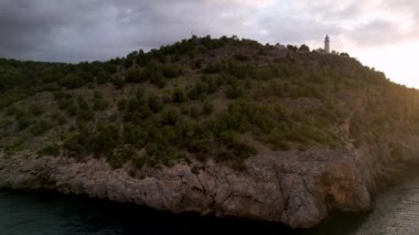 Popüler yaz mevsiminin 4K Aerial Drone videosu, uçurumların üzerinde gün batımı bir deniz feneri ve büyük bir liman dolusu martıların uçtuğu altın saat. Port de Soller, Mallorca