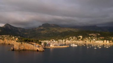 Popüler yaz mevsiminin 4K Aerial Drone videosu, uçurumların üzerinde gün batımı bir deniz feneri ve büyük bir liman dolusu martıların uçtuğu altın saat. Port de Soller, Mallorca