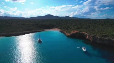 4K Hava Aracı 'nın en inanılmaz turkuaz mavi su renginde kayalık bir formasyon ve güneşli bir yaz gününde demirlenmiş tekneler Cala Varques, Mallorca' da gözlerden uzak bir plaj.