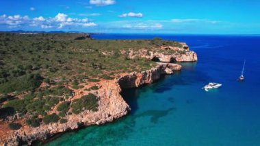 4K Hava Aracı 'nın en inanılmaz turkuaz mavi su renginde kayalık bir formasyon ve güneşli bir yaz gününde demirlenmiş tekneler Cala Varques, Mallorca' da gözlerden uzak bir plaj.