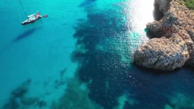 4K Hava Aracı 'nın en inanılmaz turkuaz mavi su renginde kayalık bir formasyon ve güneşli bir yaz gününde demirlenmiş tekneler Cala Varques, Mallorca' da gözlerden uzak bir plaj.