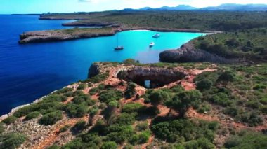 4K Hava Aracı 'nın en inanılmaz turkuaz mavi su renginde kayalık bir formasyon ve güneşli bir yaz gününde demirlenmiş tekneler Cala Varques, Mallorca' da gözlerden uzak bir plaj.