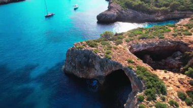 4K Hava Aracı 'nın en inanılmaz turkuaz mavi su renginde kayalık bir formasyon ve güneşli bir yaz gününde demirlenmiş tekneler Cala Varques, Mallorca' da gözlerden uzak bir plaj.