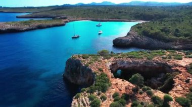 4K Hava Aracı 'nın en inanılmaz turkuaz mavi su renginde kayalık bir formasyon ve güneşli bir yaz gününde demirlenmiş tekneler Cala Varques, Mallorca' da gözlerden uzak bir plaj.