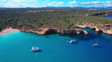 4K Hava Aracı 'nın en inanılmaz turkuaz mavi su renginde kayalık bir formasyon ve güneşli bir yaz gününde demirlenmiş tekneler Cala Varques, Mallorca' da gözlerden uzak bir plaj.