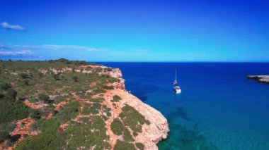 4K Hava Aracı 'nın en inanılmaz turkuaz mavi su renginde kayalık bir formasyon ve güneşli bir yaz gününde demirlenmiş tekneler Cala Varques, Mallorca' da gözlerden uzak bir plaj.