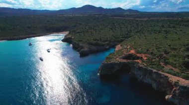 4K Hava Aracı 'nın en inanılmaz turkuaz mavi su renginde kayalık bir formasyon ve güneşli bir yaz gününde demirlenmiş tekneler Cala Varques, Mallorca' da gözlerden uzak bir plaj.