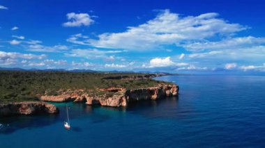 4K Hava Aracı 'nın en inanılmaz turkuaz mavi su renginde kayalık bir formasyon ve güneşli bir yaz gününde demirlenmiş tekneler Cala Varques, Mallorca' da gözlerden uzak bir plaj.