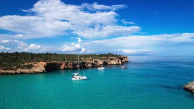 4K Hava Aracı 'nın en inanılmaz turkuaz mavi su renginde kayalık bir formasyon ve güneşli bir yaz gününde demirlenmiş tekneler Cala Varques, Mallorca' da gözlerden uzak bir plaj.