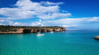 4K Hava Aracı 'nın en inanılmaz turkuaz mavi su renginde kayalık bir formasyon ve güneşli bir yaz gününde demirlenmiş tekneler Cala Varques, Mallorca' da gözlerden uzak bir plaj.