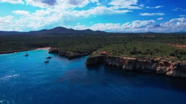 4K Hava Aracı 'nın en inanılmaz turkuaz mavi su renginde kayalık bir formasyon ve güneşli bir yaz gününde demirlenmiş tekneler Cala Varques, Mallorca' da gözlerden uzak bir plaj.