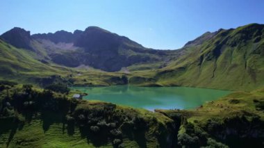 4K Hava Aracı Schrecksee Dağı 'nın en güzel dağ gölünün videosu Bavyera Alpleri' nde güneşli bir günde yemyeşil çimlerle beslenen ineklerle mavi gökyüzü ve etrafındaki kayalık tepelerle çevrili.