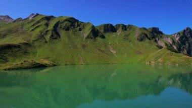 4K Hava Aracı Schrecksee Dağı 'nın en güzel dağ gölünün videosu Bavyera Alpleri' nde güneşli bir günde yemyeşil çimlerle beslenen ineklerle mavi gökyüzü ve etrafındaki kayalık tepelerle çevrili.