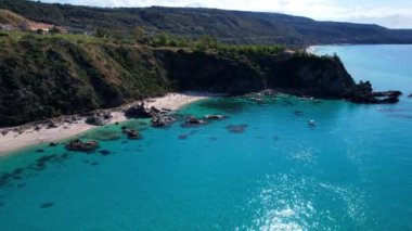 Dünyanın en güzel plajlarından birinin 4K Hava Aracı videosu. Turkuaz berrak mavi su ve güneşli bir yaz gününde büyük kayaları olan beyaz kum. Marinella di Zambrone Paradiso Tropea İtalya